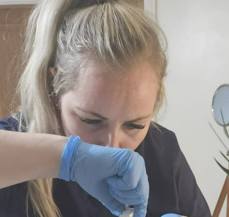 Alicia Marsland at work in the treatment room: navy scrubs, blue nitrile gloves, her attention entirely on what her hands are doing.
