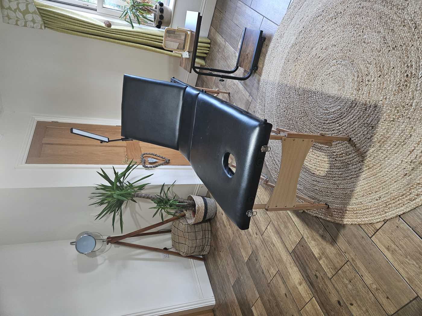 The treatment room at Glebe Farm: a single couch on a jute rug, a wooden floor, a yucca by the window and daylight from one side.